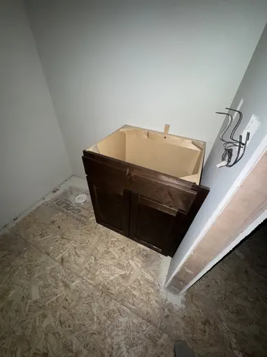 A compact wood vanity cabinet before counter installation, view 1.