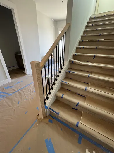 Stair-skirt fitting followed by wood handrails and black balusters on the same straight flight, view 6.