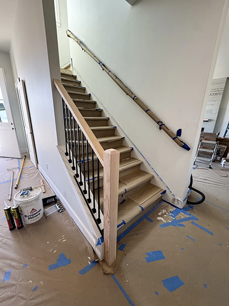 Stair-skirt fitting followed by wood handrails and black balusters on the same straight flight, view 7.