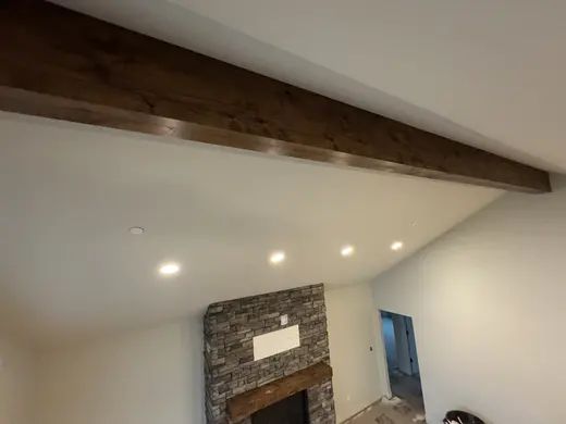 Wood ceiling beam and mantel installation in a vaulted room with a stone fireplace, view 6.