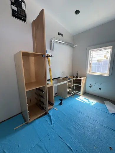 Natural wood kitchen cabinets and an island during installation over blue floor protection, view 1.
