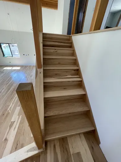 Wood stair treads and risers during installation; railing work remains, view 1.