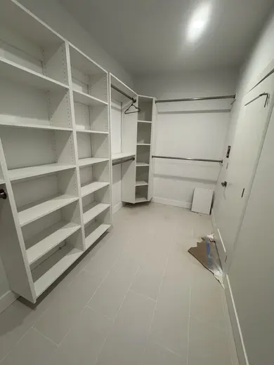 White shelves and hanging rails arranged around a walk-in closet, view 2.